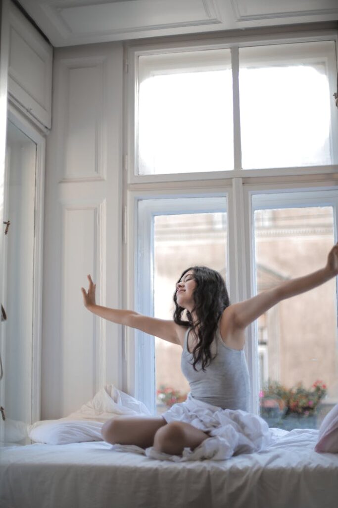 A woman enjoys the morning sunlight as she stretches in bed, feeling relaxed and refreshed.